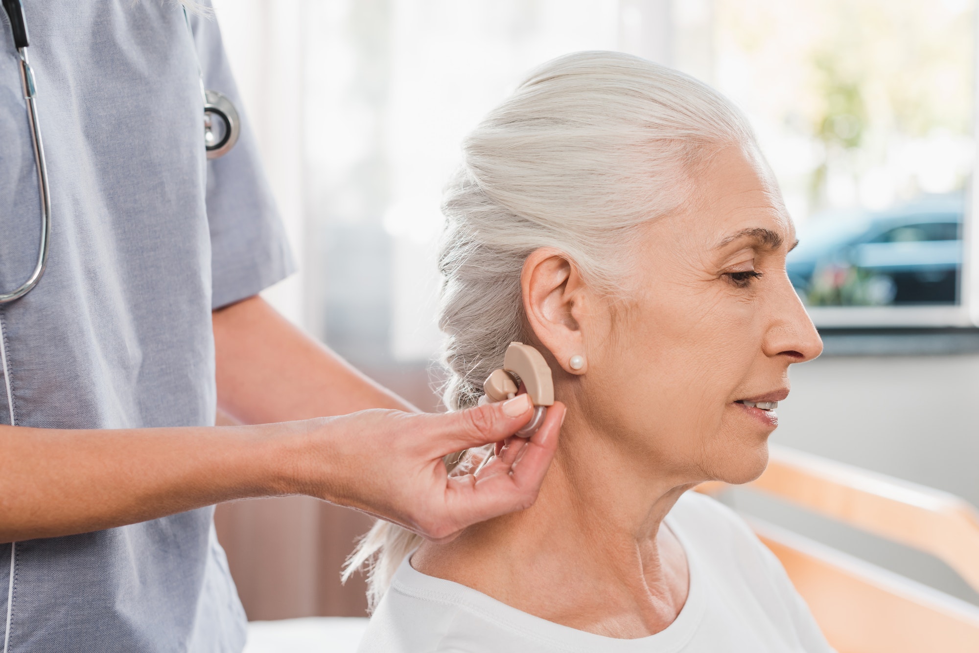 cropped shot of nurse wearing hearing aid to senior patient